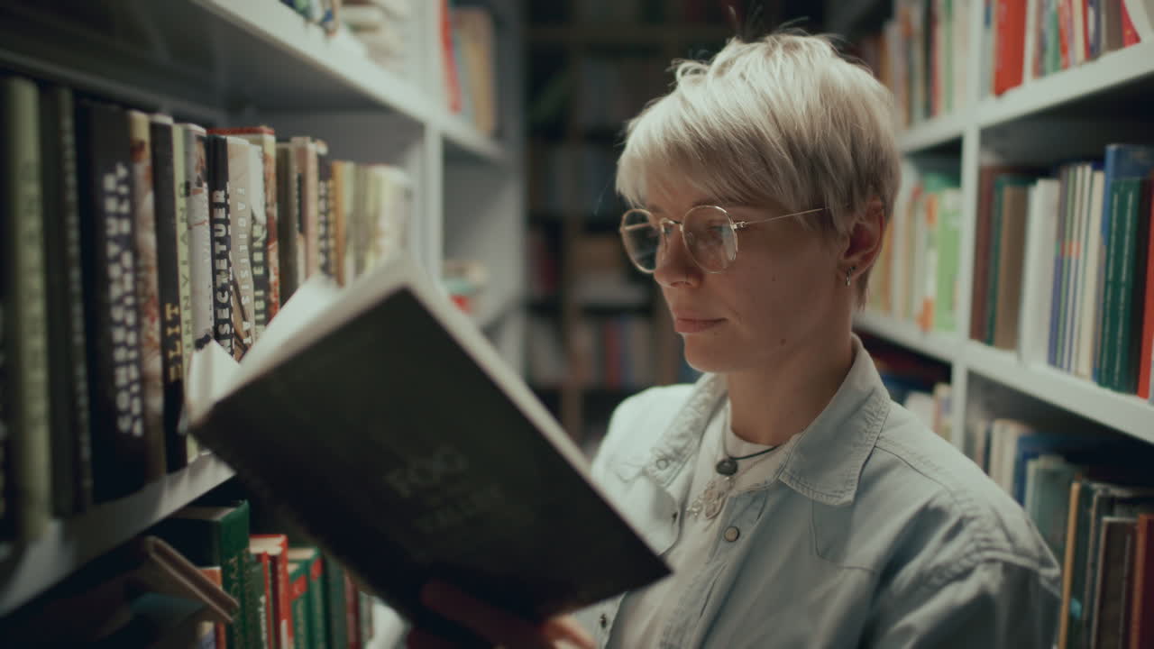 mujer joven leyendo un libro entre los estantes durante una visita a la biblioteca