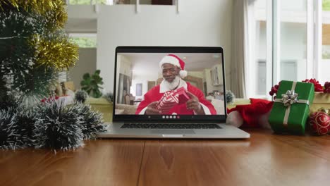 Smiling-african-american-man-wearing-santa-claus-costume-on-christmas-video-call-on-laptop