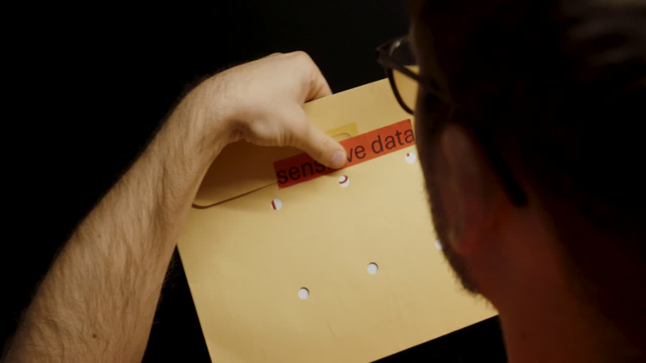 A worker carefully seals a brown envelope labeled “sensitive data,” symbolizing data protection and confidentiality in the workplace