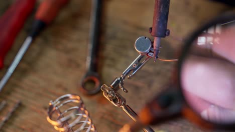 close-up of the hands of a caucasian man using a soldering tin iron while soldering some electrical contacts while using a magnifying glass