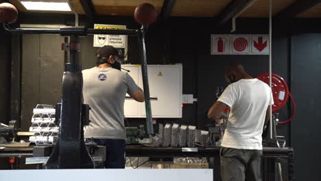 White-male-looking-over-to-a-African-American-man-working-in-a-shop-with-masks-on-in-slow-motion