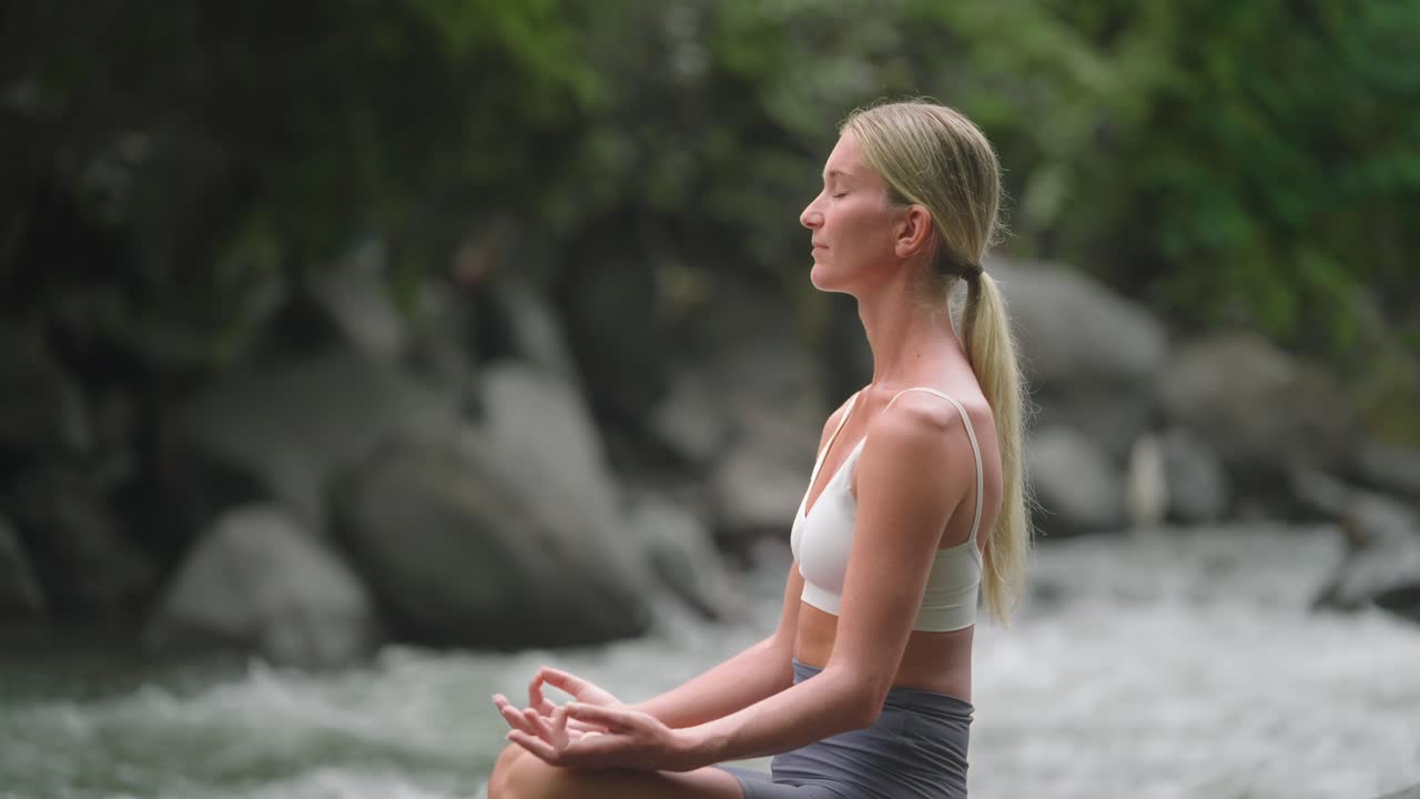 elegante mujer rubia con los ojos cerrados en pose de yoga al aire libre en la naturaleza de bali