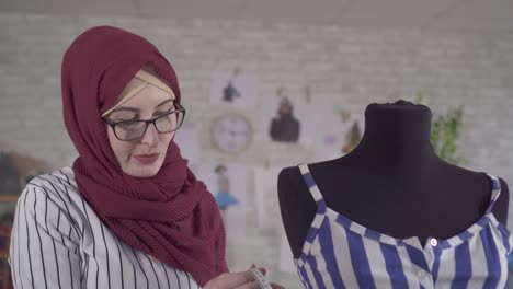 young muslim woman fashion designer in national headscarf makes a fitting on a blue dress on a mannequin in a modern studio