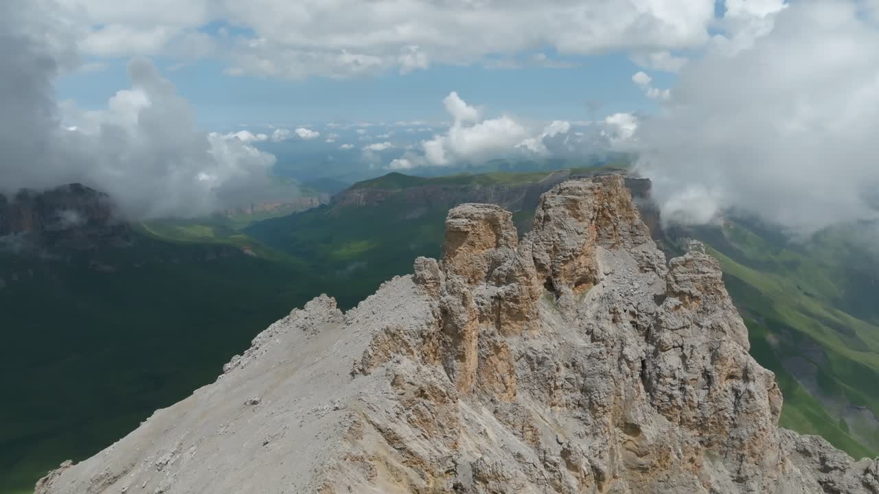Filmato aereo di una cresta calcarea frastagliata e ripidi pendii montani con nuvole basse e valli illuminate dal sole vicino al Monte Naudzhidza, Monti del Caucaso, Russia
