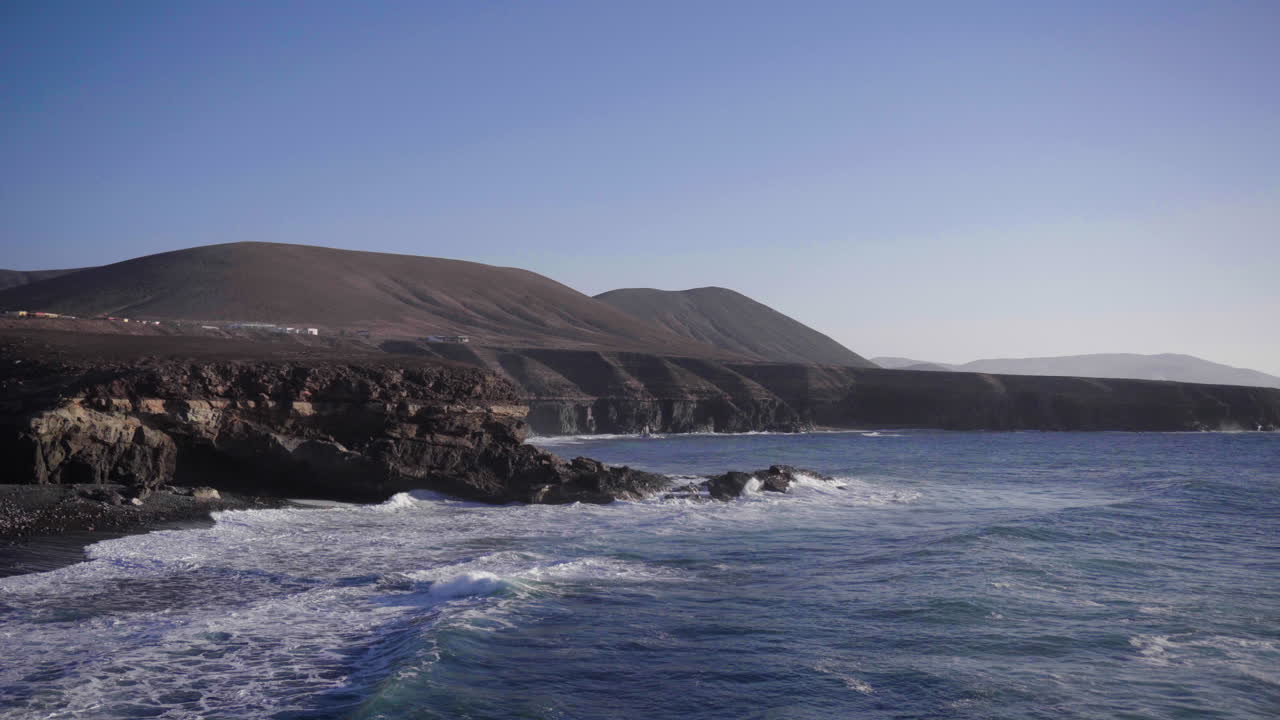 Big waves rolling in at the coast of Fuerteventura, Canary Islands, with large mountains in the background