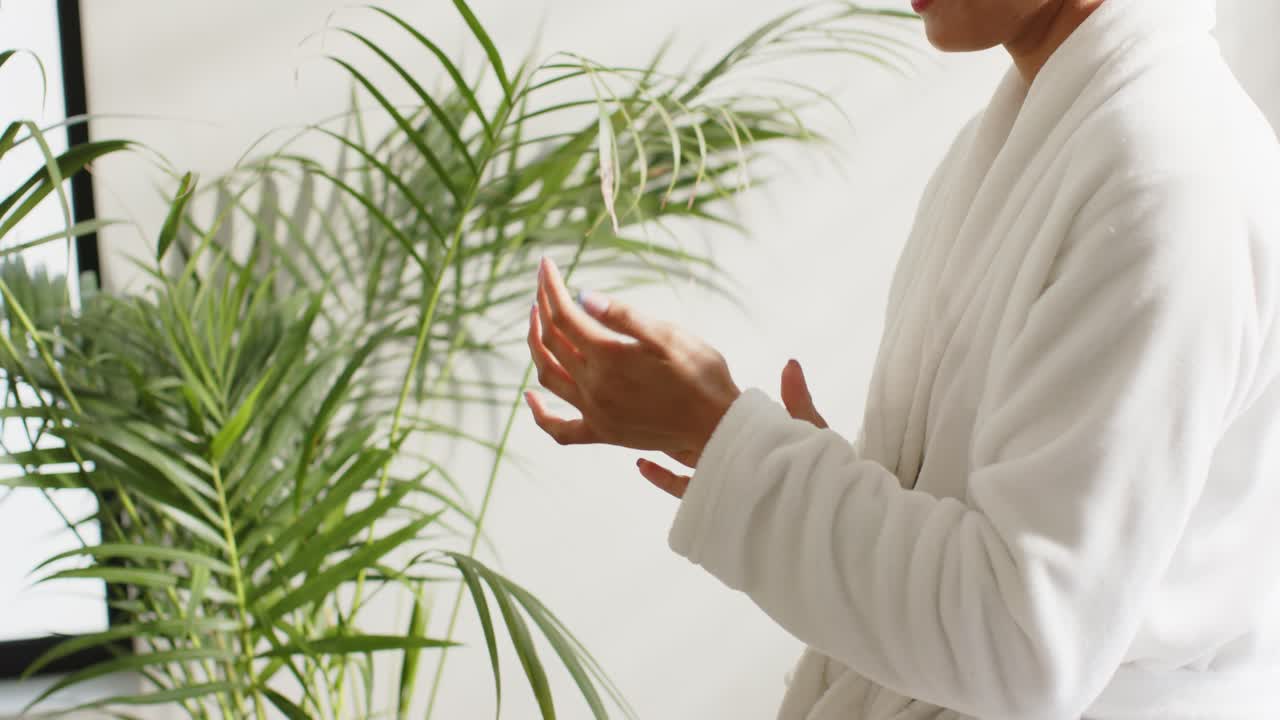 Kvinne skrur av lokket på kremen og smører hendene med lotion for å hydrere dem ved siden av en pottepalme