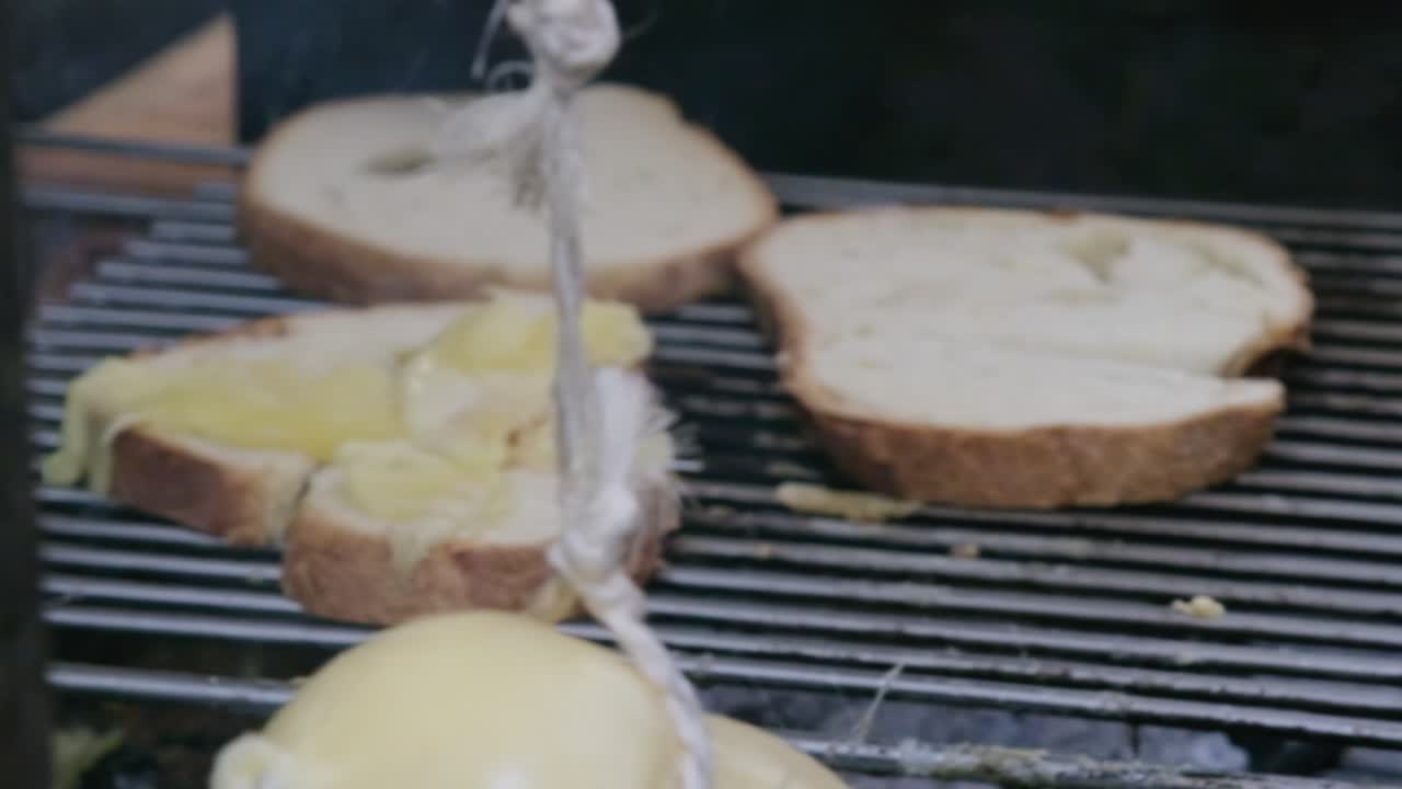 Slow motion of two caciocavallo cheeses swaying like dancers as a hand reaches to select one. They bounce and twist on strings, creating mesmerizing movement against rustic kitchen backdrop