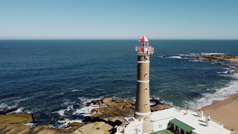 Toma-Aérea-Constante-Del-Faro-Con-El-Océano-Y-La-Costa-En-Segundo-Plano