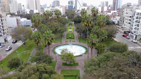 Drone-video-of-a-park-with-many-trees-including-pine-trees,-and-a-big-empty-shut-off-water-fountain