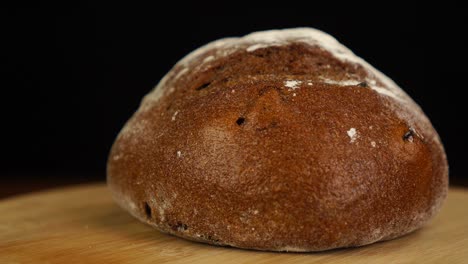 whole loaf of sourdough bread rotation in slow motion on wooden table against black background