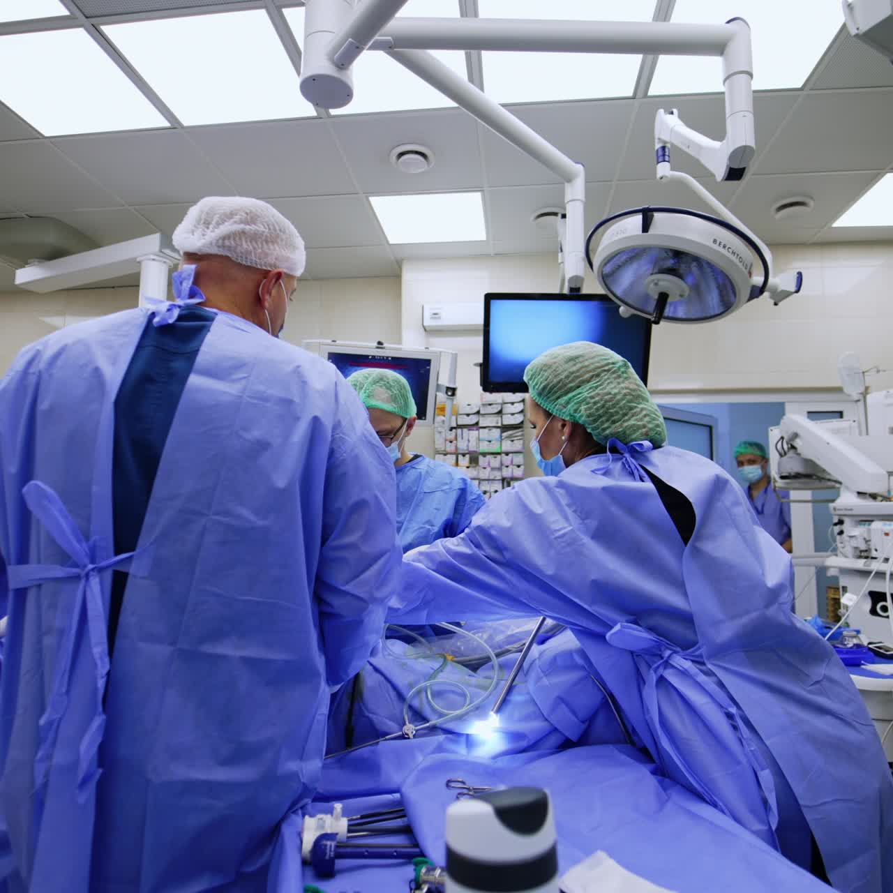 Surgical specialists stand around the patient at operational table. Modern medical equipment in the room around