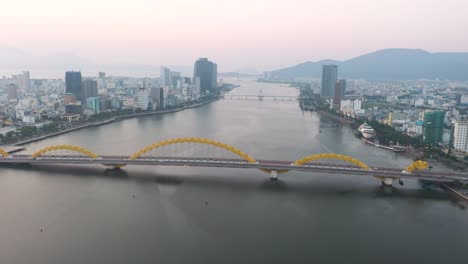 Amazing-wide-aerial-of-iconic-Dragon-Bridge-Cau-Rong,-traffic-and-city-skyline-during-sunset-in-Danang,-Vietnam