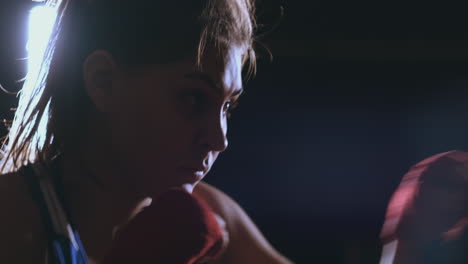 a beautiful woman boxer trains in a dark gym and works out punches in slow motion. side view. steadicam shot