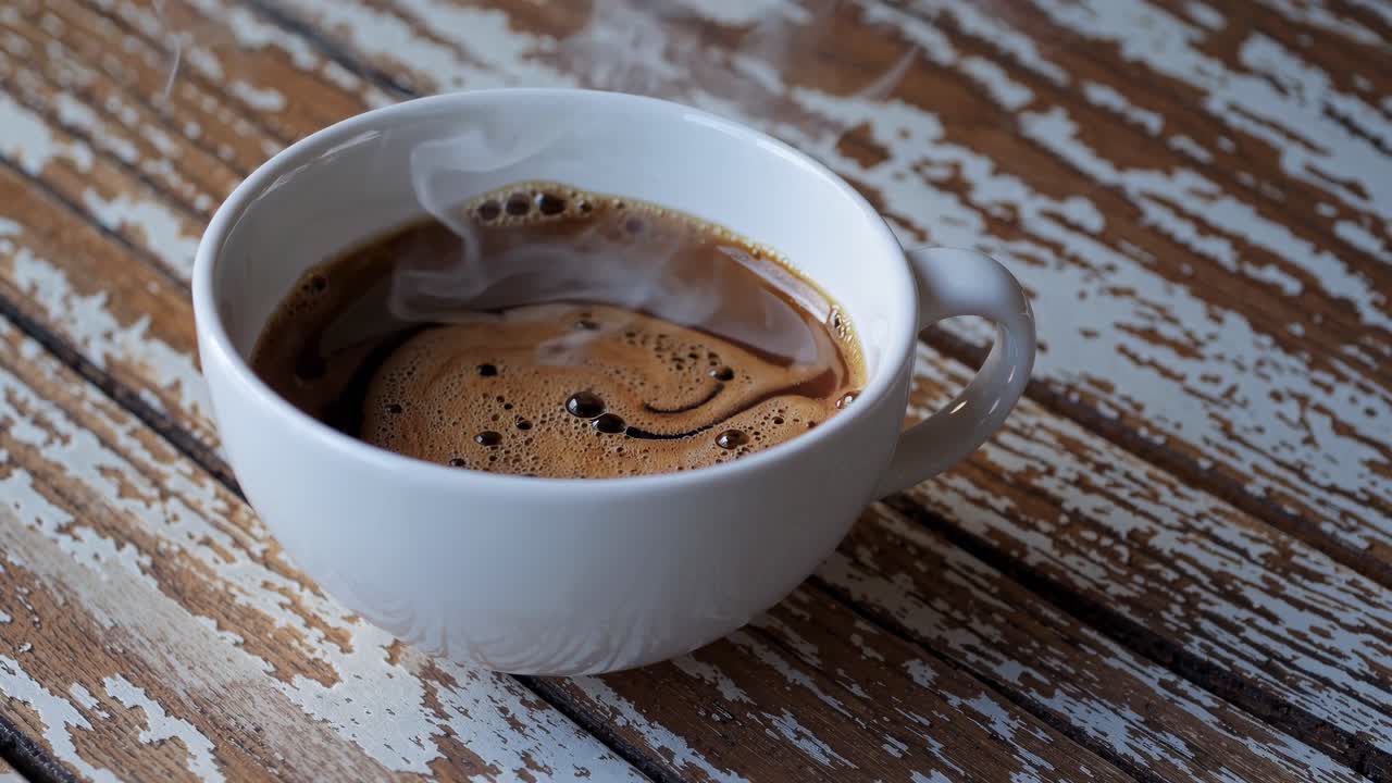 Close-up video of steaming coffee in a white cup on a rustic wooden table, captured from a high