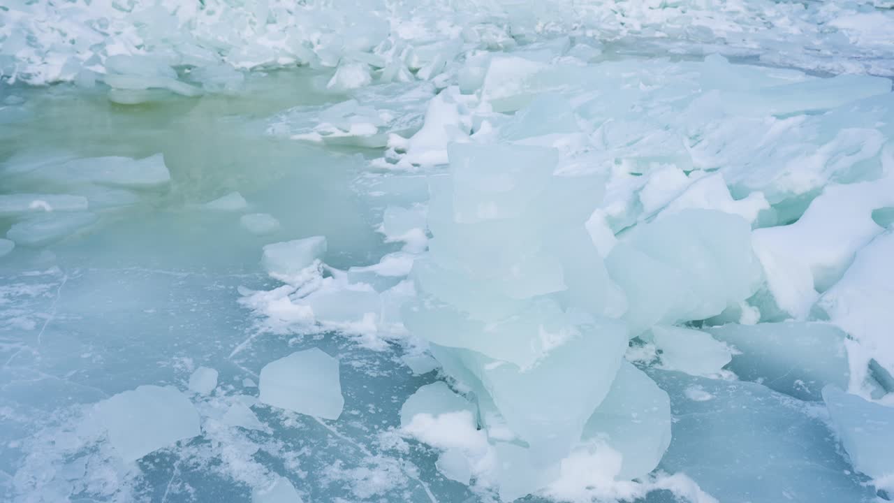 Primo piano di lastre di ghiaccio blu traslucide e blocchi spezzati accanto a una pallida pozza d'acqua di disgelo su mare ghiacciato. Drammatica texture invernale che mostra fragili condizioni di disgelo con spazio per il testo