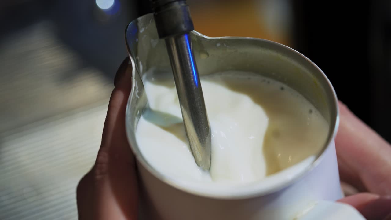 Hot milk pouring from coffee machine. Making fresh coffee with milk. Process of cappuccino preparation. Close-up.