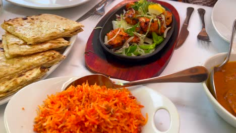 traditional indian tandoori chicken with onions on a very hot plate, butter chicken, cheese naan bread and coconut rice in a restaurant, authentic asian food, 4k shot