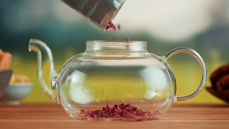 pouring dried rose petals into a glass teapot for brewing herbal tea