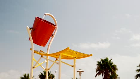 Water-poured-from-huge-bucket-over-people-at-water-park,-slow-motion