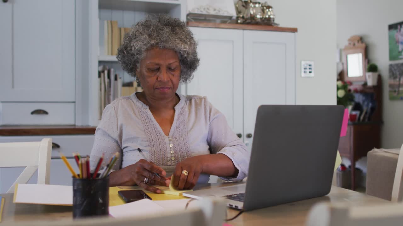 Senior african american woman sticking memo notes on her laptop at home