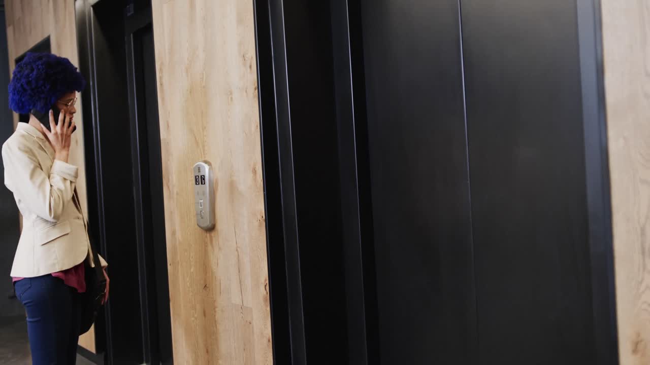 mujer de negocios biracial con afro azul hablando en teléfono inteligente y usando ascensor, cámara lenta