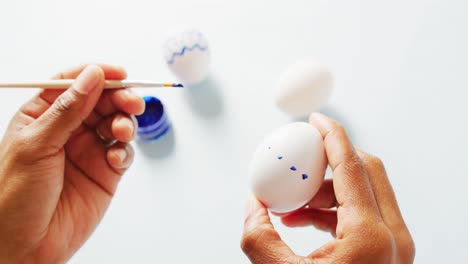 hands painting white eggs using brush with blue paint on white background