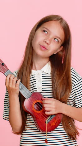 little child girl kid playing toy ukulele smiling while enjoying imaginary concert performance