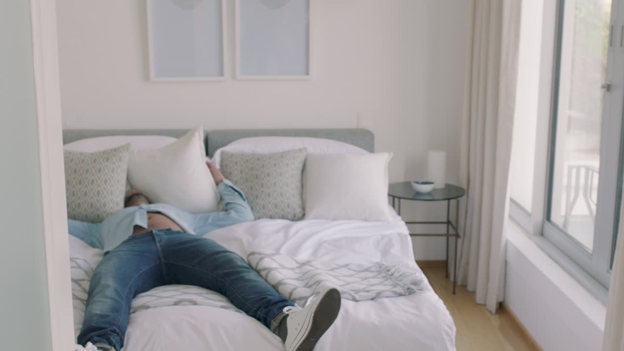 피곤한 남자가 침대에 뛰어다니며 여행 후 휴식을 취하고 집에서 휴식을 즐기고 있습니다.