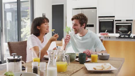 video of happy diverse couple eating breakfast together in kitchen