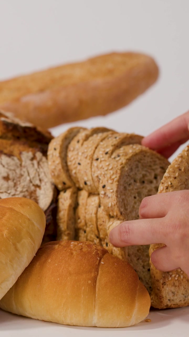 Primo piano di mani che selezionano pane multicereali a fette da una varietà di pagnotte fresche di panetteria.