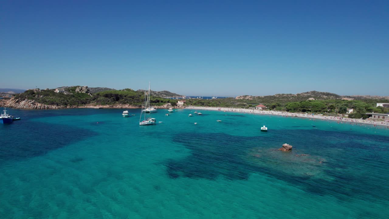 Toma aérea lateral izquierda con inclinación ascendente de barcos de crucero anclados en la isla de Cerdeña, cerca de la costa, disfrutando del verano en el mar Mediterráneo.