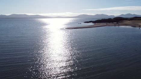 Aerial-view-Ynys-Llanddwyn-Welsh-island-coast-with-shimmering-ocean-and-misty-Snowdonia-mountain-range-across-the-sunrise-skyline