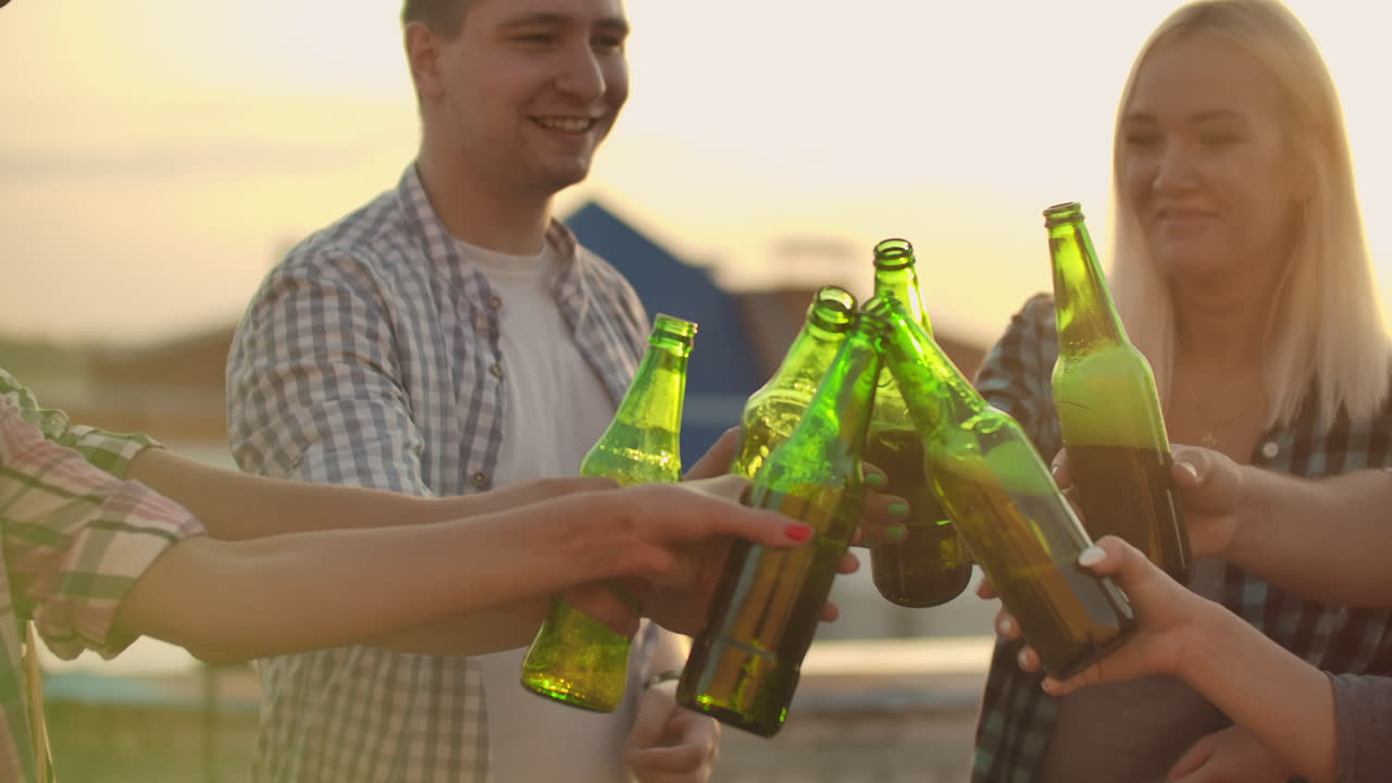 la compañía de jóvenes chillando vasos y bebiendo cerveza en la fiesta con amigos en el techo