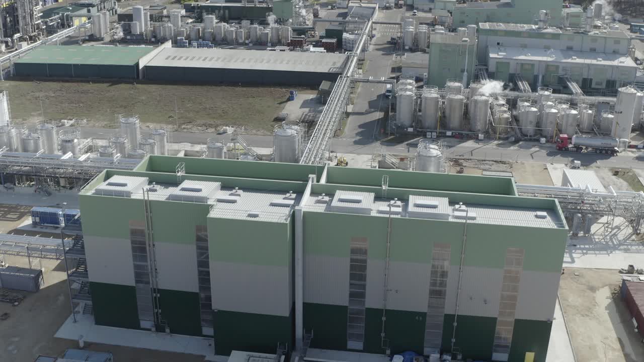 Aerial view of two large, modern industrial buildings within a sprawling factory complex with tanks and piping, Castets, France