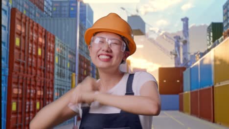 close up de una trabajadora asiática que usa gafas de protección y casco de seguridad bailando mientras está de pie en el almacén del patio de contenedores