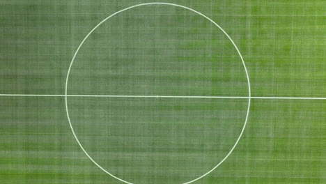 top-down-aerial-view-of-a-sports-field,-likely-a-soccer-pitch,-with-clearly-marked-white-boundary-lines-and-center-circle-on-the-green-grass