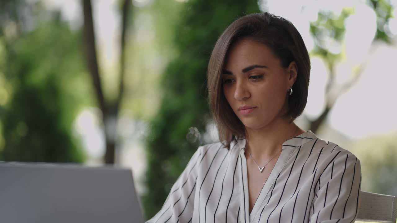mujer de negocios morena de etnia hispana trabaja remotamente mientras está sentada en un café de verano en un día soleado.