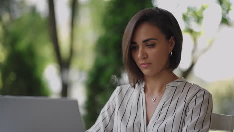 mujer de negocios morena de etnia hispana trabaja remotamente mientras está sentada en un café de verano en un día soleado.