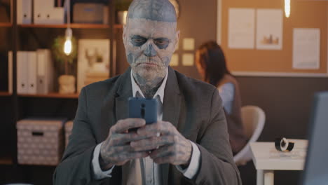 man with skull tattoo using smartphone in office