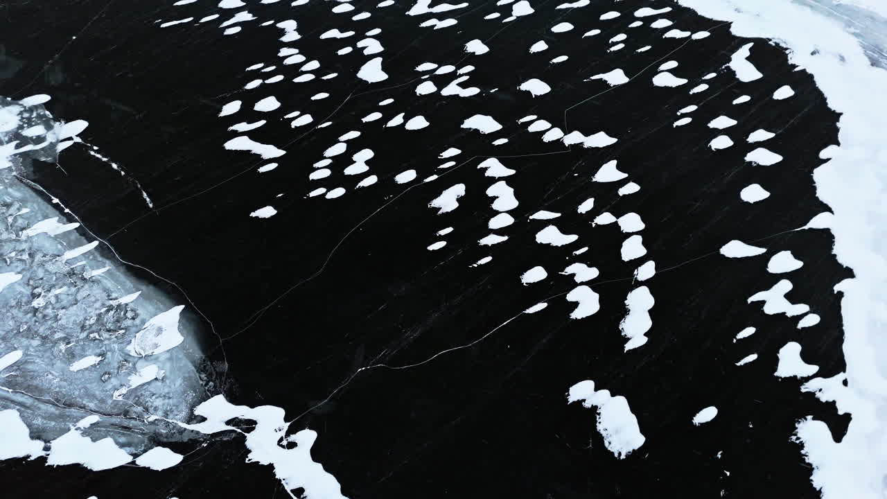 Fiordo ghiacciato a Tromsø con ghiaccio scuro e crepato e chiazze di neve sparse, vista aerea.