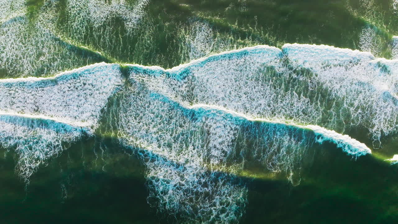 Beautiful relaxing movement of foamy waves on the surface of ocean. Descending drone footage over the deep green waters.