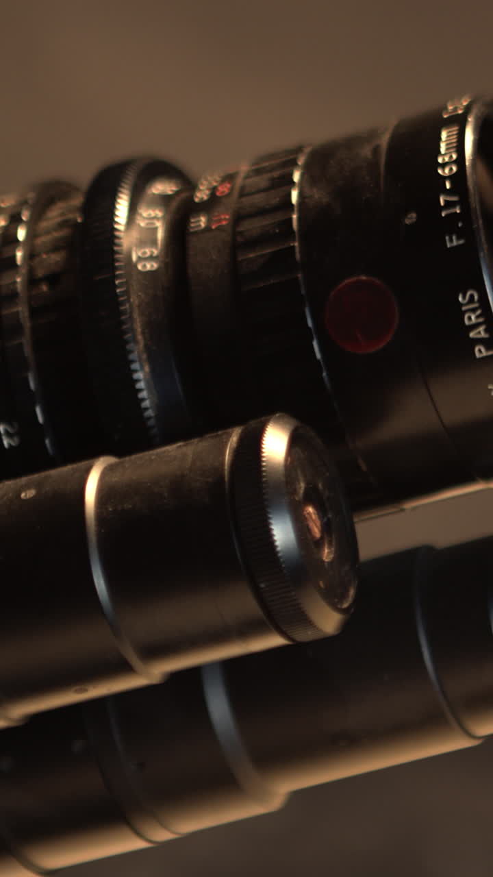 Primo piano cinematografico con carrello che rivela le ottiche di una cinepresa retrò in un ambiente di studio scuro. Ideale per temi di produzione cinematografica, produzione e industria dei media.