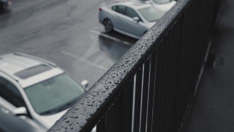 a close up shot of rain dripping onto a metal handrail for a walkway with a parking lot in the background