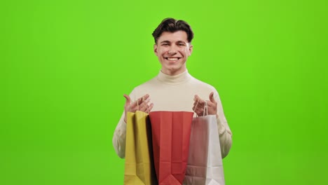 un hombre está mirando en bolsas de compras. está sonriendo y regocijándose. está de pie sobre un fondo verde. pantalla verde. 4k.
