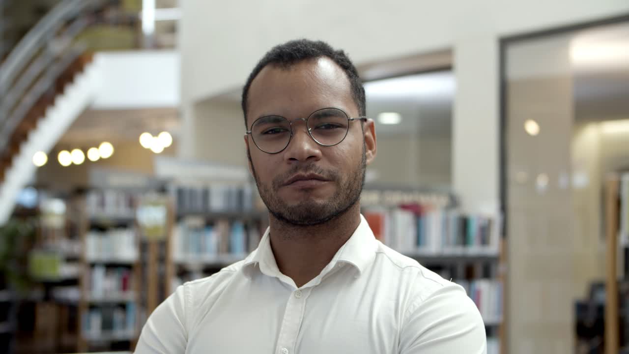Hombre afroamericano sonriente que presenta en la biblioteca pública