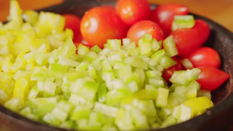 extreme close up handheld shot capturing freshly diced green bell pepper and organic cherry tomato in mini cast iron pan