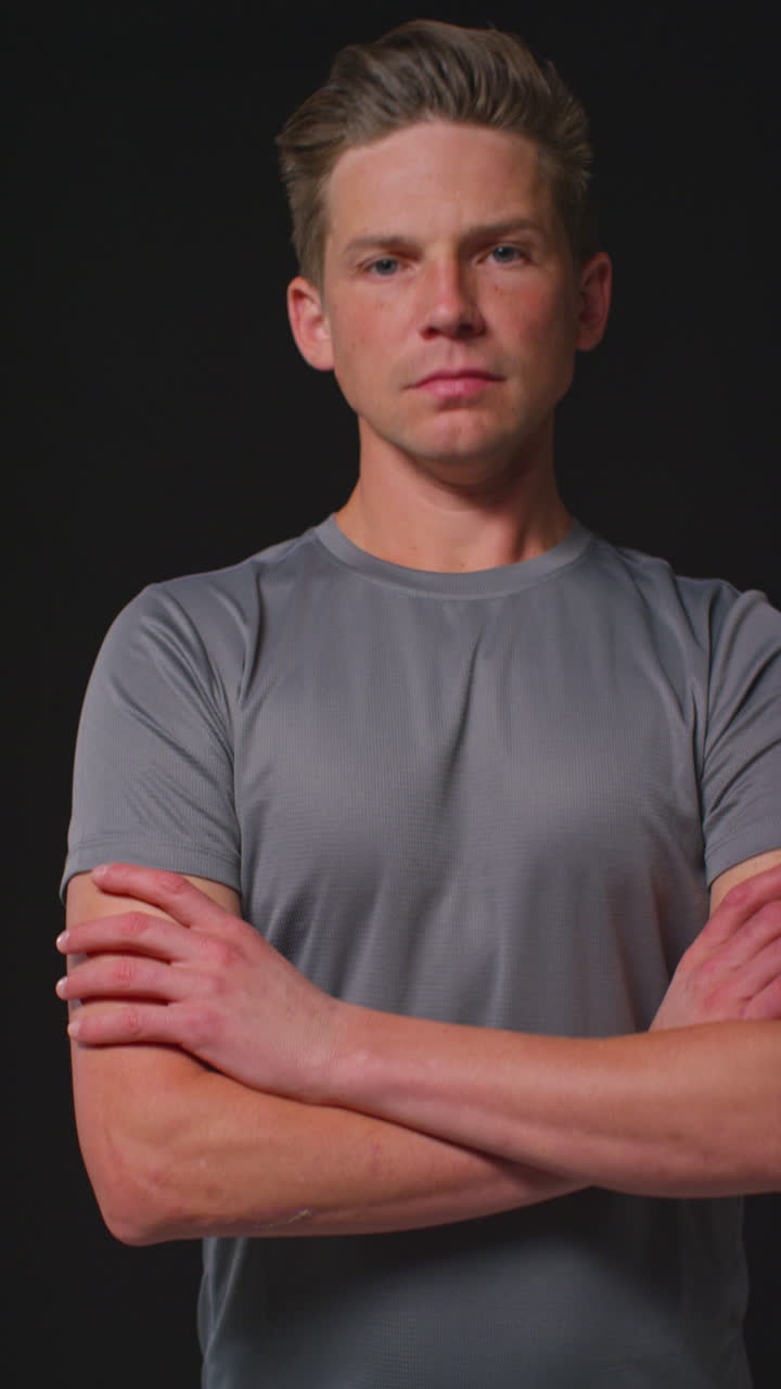 Vertical Video Portrait Of Serious Male Athlete Wearing Fitness Clothing Walking Towards Camera And Into Focus Training For Sports Event Against Black Studio Background