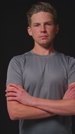 vertical video portrait of serious male athlete wearing fitness clothing walking towards camera and into focus training for sports event against black studio background