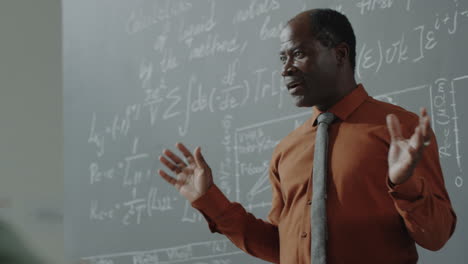 african american professor lecturing in front of a chalkboard filled with equations