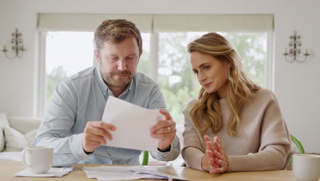 worried couple sitting at table at home reviewing domestic finances opening bill